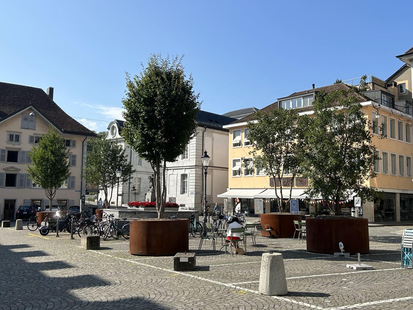 Aktuelle Projektbeispiele von Mobile Green, Einsatz in Solothurn (SO) mit über 17'000 Einwohnern: Seit dem 16.08.2024 stehen auf dem Kreuzackerplatz fünf Grossbäume mit einem Wassertankvolumen von je 540 Liter. Auf der öffentlichen Fläche finden unter anderem auch Festivals und Events statt, im Sommer werden Buvetten betrieben. © Copyright Bauer Baumschulen| Digitale Medienmappe «Mobile Begrünungen schützen Städte vor Überhitzung – Schweizer Innovation zum Patent angemeldet», Bauer Baumschulen