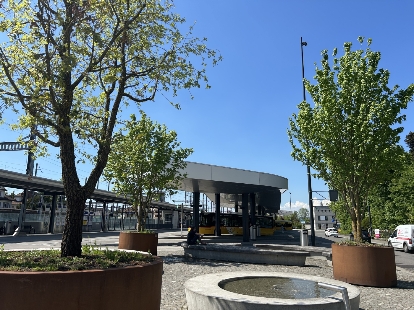 Aktuelle Projektbeispiele von Mobile Green, Einsatz in der Gemeinde Wohlen (AG) mit über 17'000 Einwohnern: In der Bahnhofsstrasse Wohlen stehen vor den Busstationen seit dem 06.11.2024 drei Grossbäume in Pflanztrögen mit Wassertanks von je 540 Liter. Die Bäume spenden auf dem öffentlichen Platz und Wartebereich wertvollen Schatten. © Copyright Bauer Baumschulen| Digitale Medienmappe «Mobile Begrünungen schützen Städte vor Überhitzung – Schweizer Innovation zum Patent angemeldet», Bauer Baumschulen