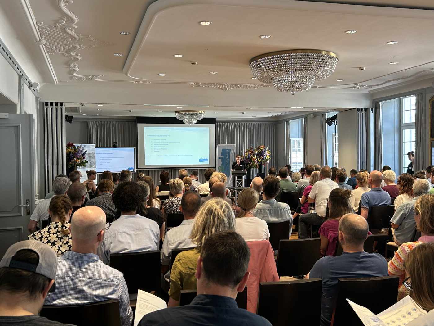 Medienbilder, Katrin Bernath, Präsidentin Trägerverein Energiestadt im vollen Saal. © Copyright Trägerverein Energiestadt| Digitale Medienmappe «Netto-Null bis 2050: Energiestadt fordert und fördert zielgerichtetes Handeln auf allen Ebenen», Trägerverein Energiestadt